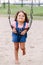 Little latin hispanic toddler girl swinging on swings at playground outside on summer day
