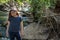 Little latina girl smiling coyly and looking down while standing in front of a stream and woods in the shade