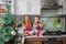 Little laughing twins sit on the table in pajamas in the Christmas decorated kitchen with an Apple. Girl with glasses