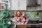 Little laughing twins sit on the table in pajamas in the Christmas decorated kitchen with an Apple. Girl with glasses