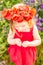 Little longhaired blonde girl in red dress at field of poppies with wreath at her head on summer sunset