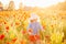 Little longhaired blonde girl in red dress at field of poppies with wreath at her head on summer sunset