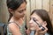 Little make up artist working outdoor, applies mascara, female face closeup. Sisters spending time together