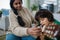 Little multiracial boy learning to play the guitar with his mother at home.