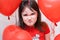 Little naughty angry girl face close up among red heart-shaped balloons