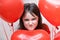 Little naughty angry girl face close up among red heart-shaped balloons