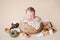 A little newborn baby sleeps in a straw basket on a beige background, there are many donuts, cakes and sweets