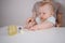 Little newborn funny baby boy learning to eat vegetable or fruit puree from glass jar with spoon. Young mother helping