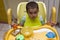 Little one-year-old kid eats porridge while sitting in his high chair