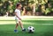 Little player: toddler boy in sports uniform playing footbal at soccer field in summer day outdoors. Child ready to kick ball