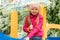 Little positive happy girl on the playground sits with a colorful umbrella from the rain.