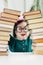 Little preschool age girl in round shape glasses and green dress behind arch made of books