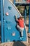 Little preschool boy in red t-shirt climbing rock wall at playground outside on summer day. Happy childhood lifestyle concept.