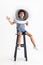 Little preschool curly boy posing in astronaut helmet sitting on a high chair isolated over white studio background.