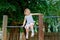 Little preschool girl climbing and hanging on outdoor horizontal bar. Cheerful girl athlete on gymnastic stick on sports