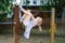 Little preschool girl climbing and hanging on outdoor horizontal bar. Cheerful girl athlete on gymnastic stick on sports