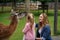 Little preschool girl and woman feeding fluffy furry alpacas lama. Happy excited child and mother feeds guanaco in a