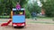 Little pretty girl in gumboots sits on wooden car at playground