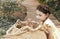 Little pretty girl in summer dress sitting outside on wooden path in front of straw basket with rabbits