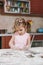 Little pretty kid girl in pink dress playing, smearing hands and drawing with flour in light kitchen at table. Child