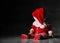 Little pretty little boy in a red sweater and santa cap, sitting on a dark background