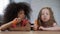 Little pretty multiracial girls sitting at table and eating carrot with appetite