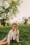 Little pretty tween girl in white clothes sitting on green grass outside in park on sunny summer day. Happy childhood and outdoor