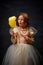 Little princess in old-fashioned dress eating, tasting bright yellow lemon flavored cotton candy against dark vintage