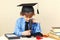 Little professor in academic hat looking through microscope at his desk