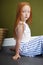 Little red-haired girl with a basket of flowers posing on an olive background. Spring portrait of a redhead girl with blue eyes.