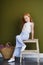 Little red-haired girl with a basket of flowers posing on an olive background. Spring portrait of a redhead girl with blue eyes.