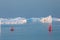 Little red sailboat cruising among floating icebergs in Disko Bay glacier during midnight sun season of polar summer. Greenland