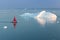 Little red sailboat cruising among floating icebergs in Disko Bay glacier during midnight sun season of polar summer. Greenland