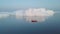 Little red sailboat cruising among floating icebergs in Disko Bay glacier during midnight sun season of polar summer. Greenland