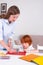 Little redhead boy with a nanny or mother or teacher sit at the table and paint with colors