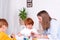 Little redhead boys with a nanny or mother or teacher sit at the table and paint with colors