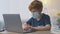 Little redhead schoolboy wearing protective medical mask studying online at home, working on laptop at workplace