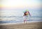 Little running girl with flying kite on beach at sunset