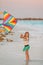 Little running girl with flying kite on tropical beach. Kid play on ocean shore.