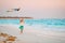 Little running girl with flying kite on tropical beach. Kid play on ocean shore.