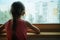 Little sad girl pensive looking through the window glass with a lot of raindrops. Sadness  and loneliness childhood concept image.