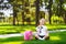 Little school girl with pink backpack sitting on grass after lessons and thinking ideas, read book and study lessons