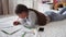 Little school girl studying at home lying on bed and writing in notebook