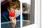 Little school kid boy by a window wearing medical mask and holding wooden heart. Valentin`s day during pandemic