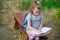 Little school miss sits having crossed legs on a park bench and something diligently writes in the notebook.