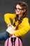 Little schoolgirl in eyeglasses puting the exercise books in pink backpack on grey studio background in fashion style clothing.