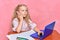 Little schoolgirl thoughtful dreaming behind laptop. online training. pink background