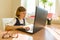 Little schoolgirl uses computer sitting at a desk at home. School, education, knowledge and children.