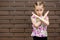 A little serious girl stands near a brick wall and shows enough or a stop sign with a gesture