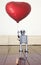 Little silver robot holding a red balloon standing